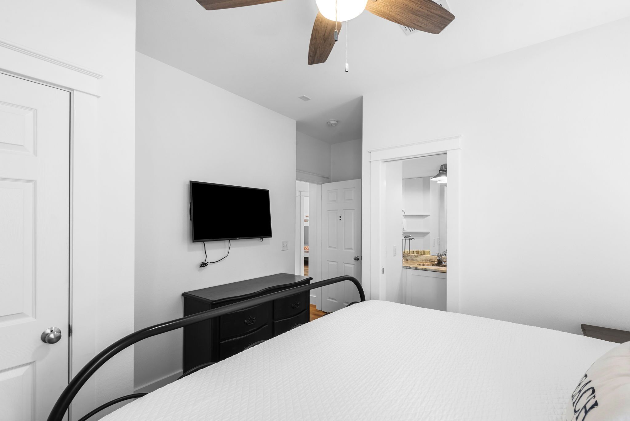 Ein Schlafzimmer mit Bett, Kommode, Wand-Fernseher und Deckenventilator.