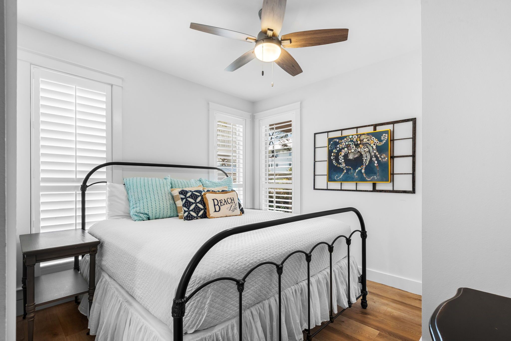 A bedroom with a bed, a nightstand, a ceiling fan, and a framed picture on the wall.