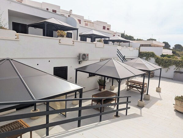 Una terraza en la azotea con múltiples toldos, mobiliario exterior y una escalera que conduce a un nivel superior.
