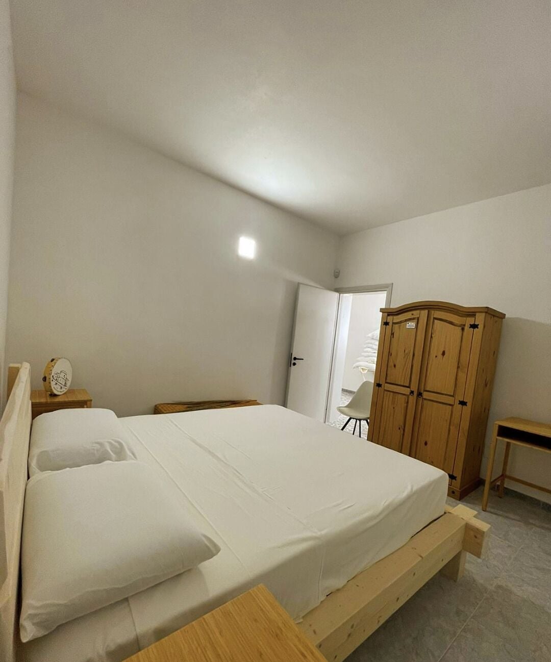 Un dormitorio con una cama individual, un armario de madera, una mesita de noche y una silla.