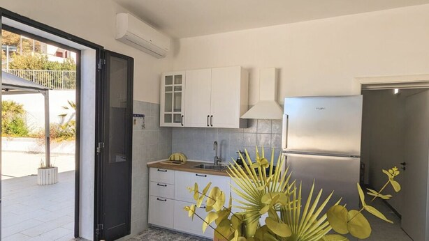 A modern kitchen with white cabinets, a built-in stove, and a dining area with a wooden table and chairs. - RESIDENCE ORIZZONTE BLU (Morciano di Leuca)