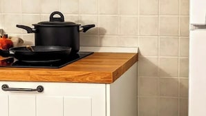 A kitchen with a wooden countertop, a black pot on an induction cooktop, and white cabinets with metal handles. - RESIDENCE ORIZZONTE BLU (Morciano di Leuca)