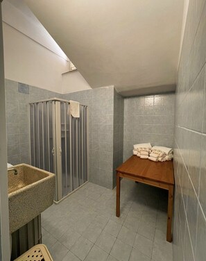 Un baño pequeño con ducha, lavamanos y una mesa con toallas.