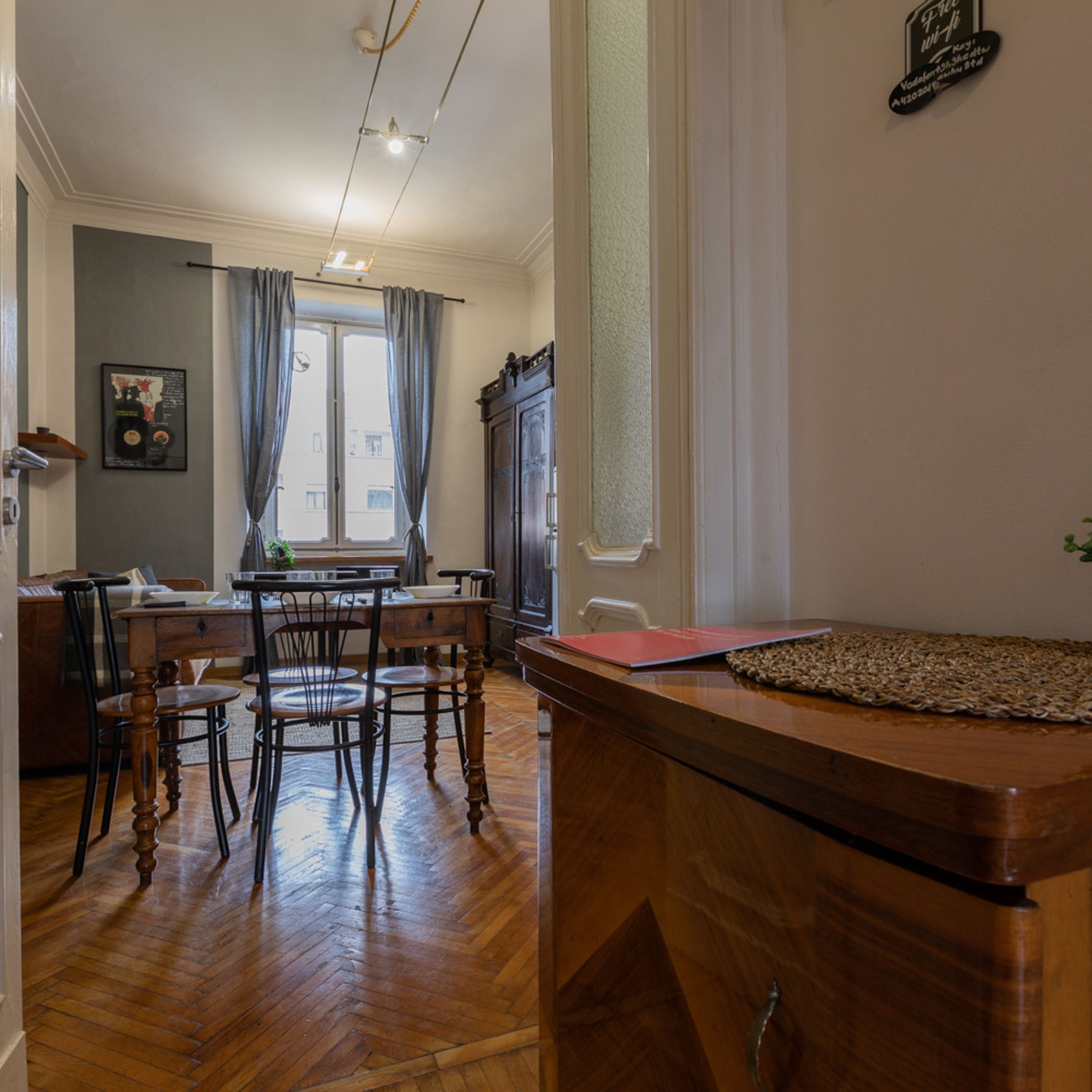 Un comedor con sillas de madera y una mesa, una cocina con refrigerador y una ventana con cortinas.