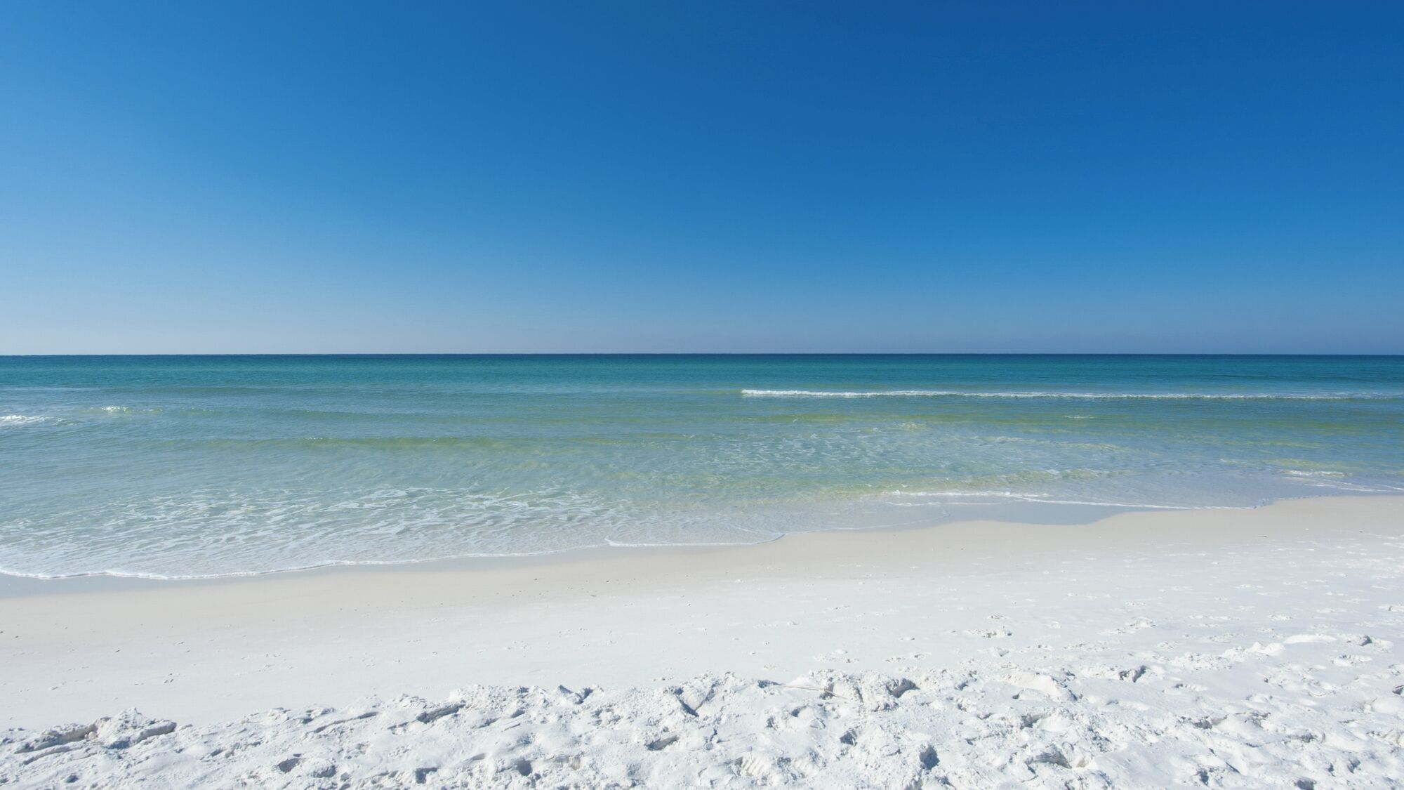 Une plage de sable blanc bordée d’une eau d’un bleu cristallin.