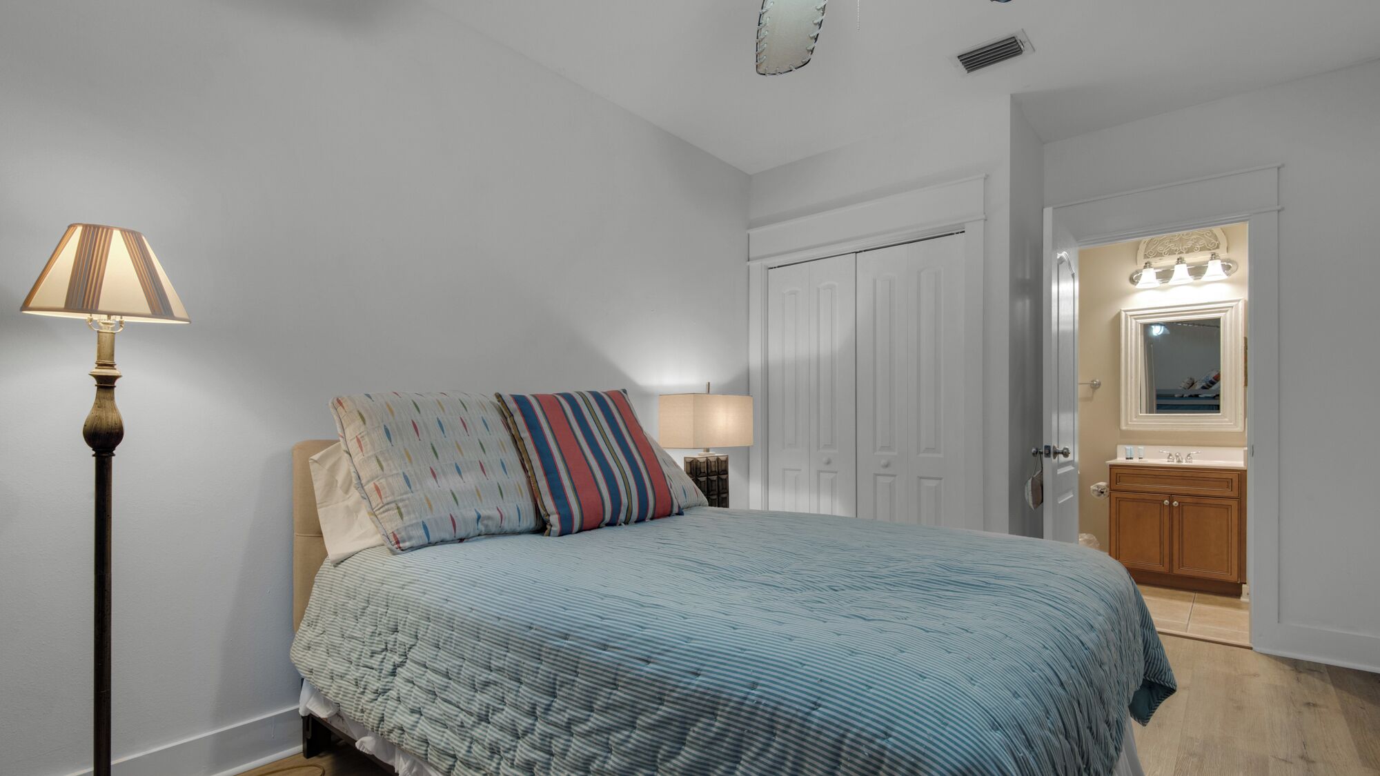Une chambre à coucher comprenant un lit, une lampe de chevet, une table de chevet, une commode et une porte donnant sur une salle de bain.