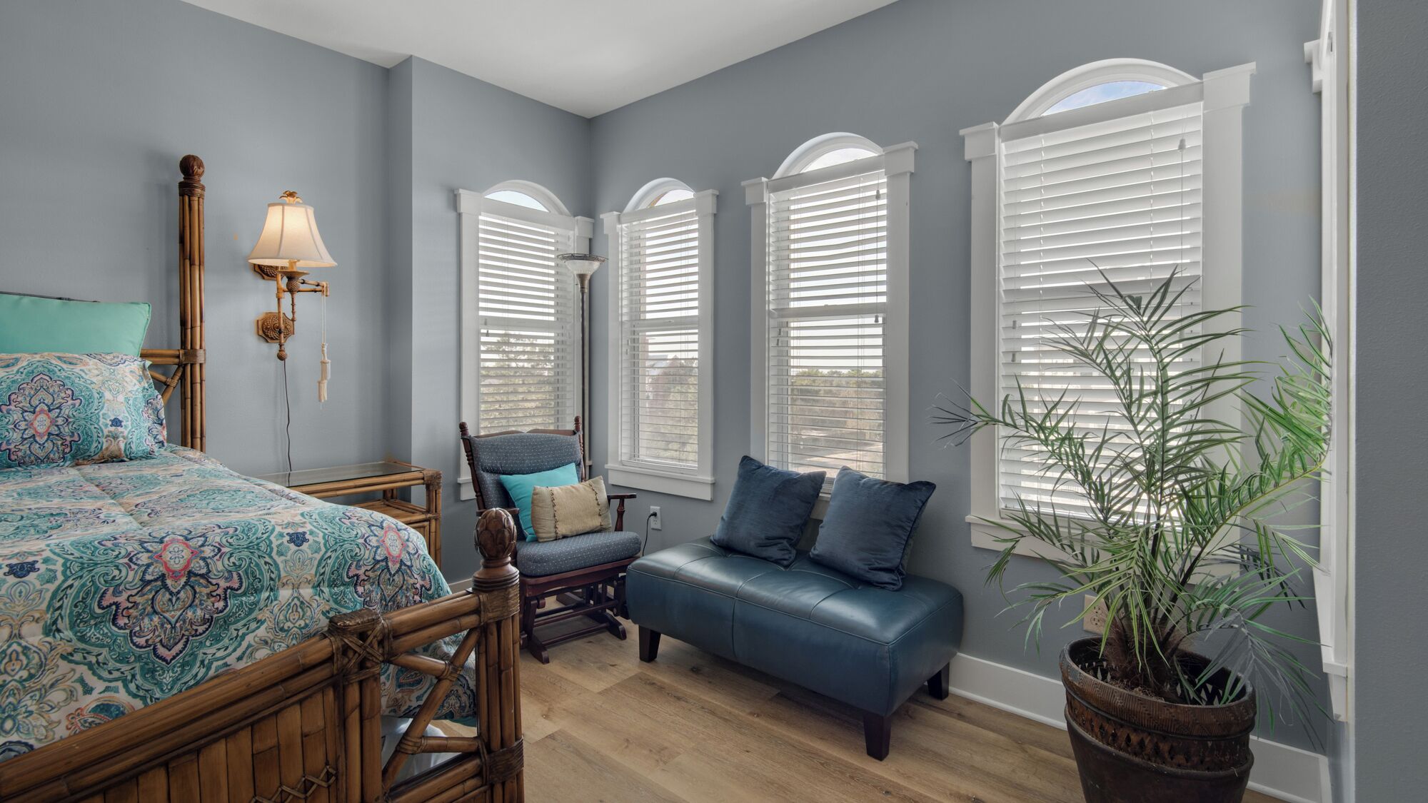 A bedroom with a bed, a chair, a bench, a lamp, and a potted plant.