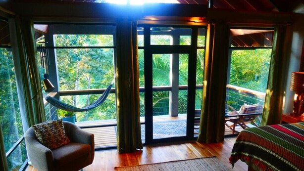 A room with a hammock, a bed, and a view of the outdoors.