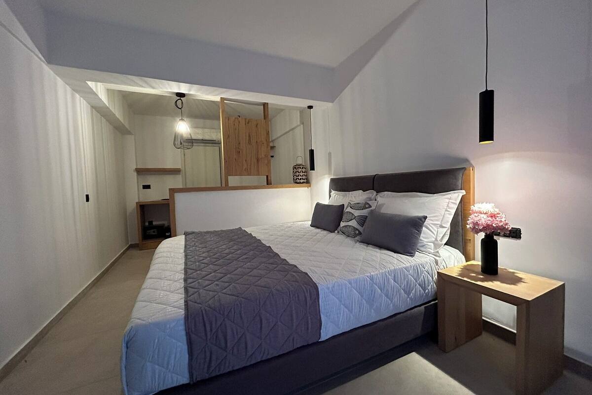 A modern bedroom with a large bed, a bedside table with a vase, and a mirror above the bed.