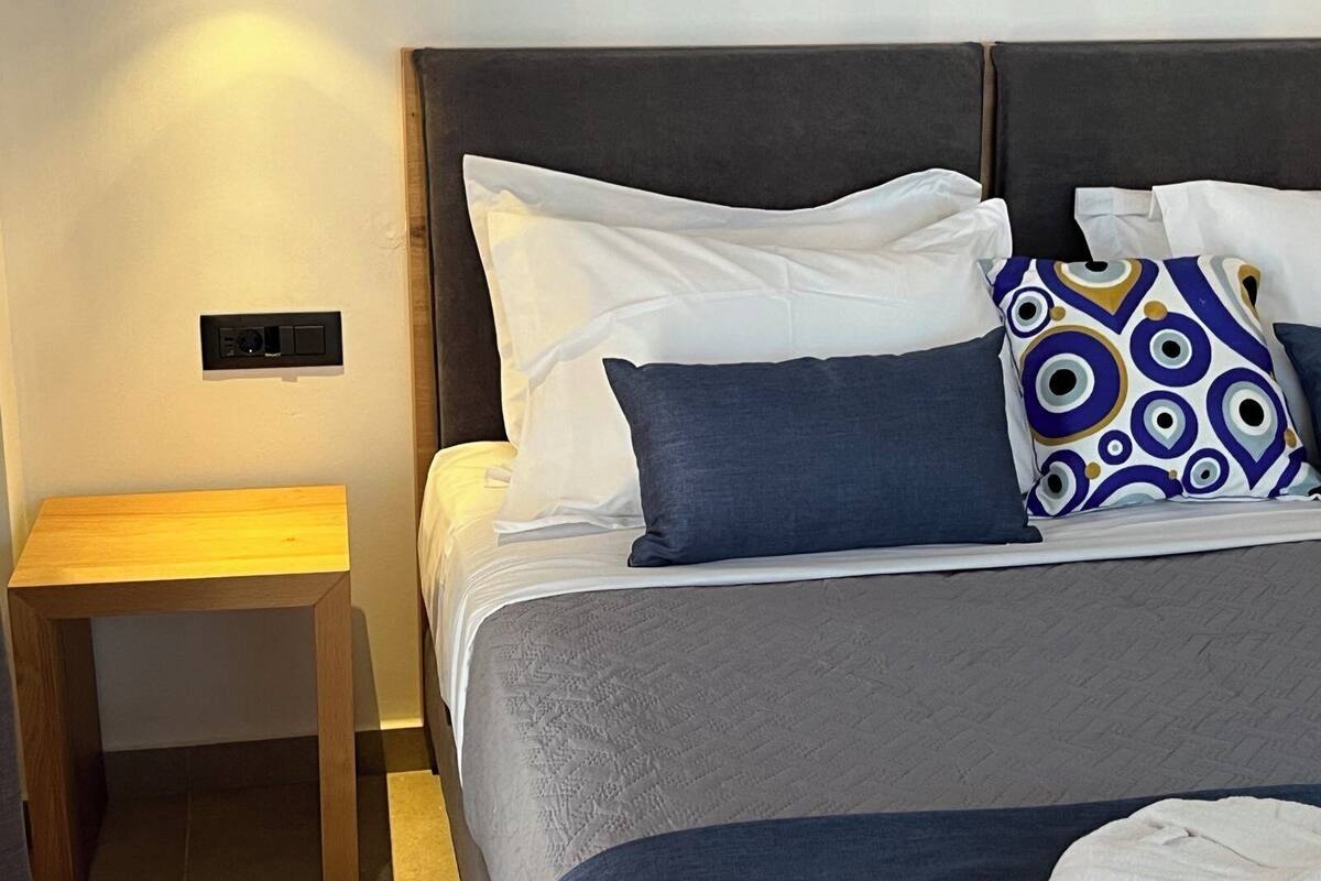 A neatly made bed with a grey bedspread and multiple pillows, including a patterned one.