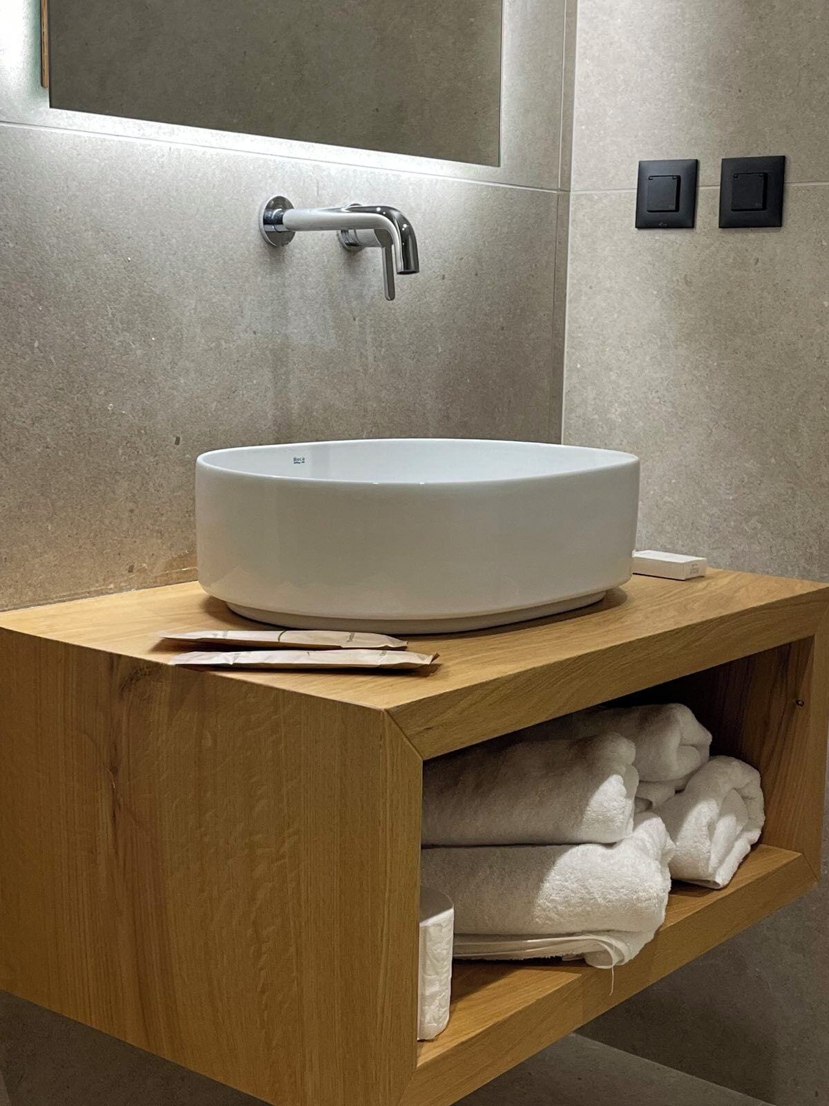 A modern bathroom with a large, round white sink, a wooden vanity, and a towel rack.