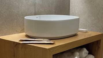 A modern bathroom with a large, round white sink, a wooden vanity, and a towel rack.