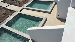 A pool area with multiple rectangular pools surrounded by white walls and a landscaped garden with rocks and sparse vegetation. - Moonlight Hotel (Santorini)