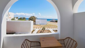 A balcony with a view of the sea and white buildings. There is a wooden table and two wicker chairs. - Moonlight Hotel (Santorini)