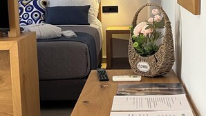 A neatly arranged hotel room with a bed, bedside table, and a small side table with a basket of flowers. - Moonlight Hotel (Santorini)