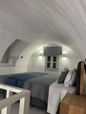 A single bedroom with a bed, a nightstand, a lamp, and a window. - Moonlight Hotel (Santorini)