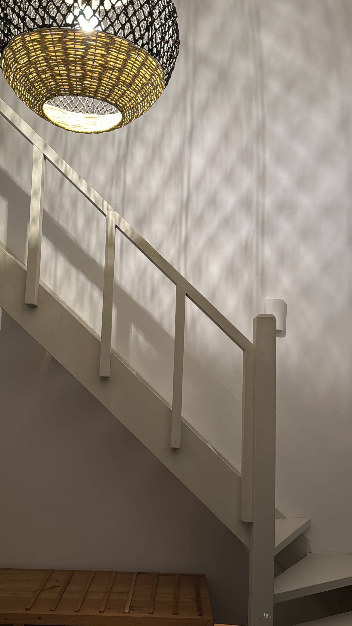 A staircase with white railings and a woven light fixture above.