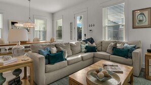 Una sala moderna con un sofá seccional color beige, una mesa de centro de madera, y un comedor con una mesa y sillas.