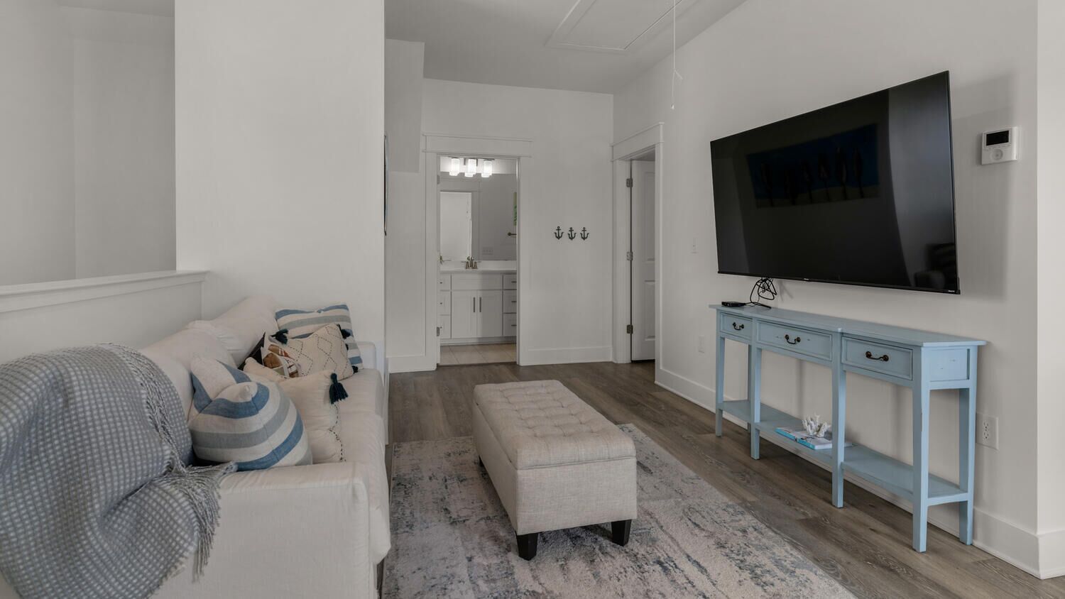 A modern living room with a large flat-screen TV, a light blue console table, a white sofa with striped cushions, and a grey rug.