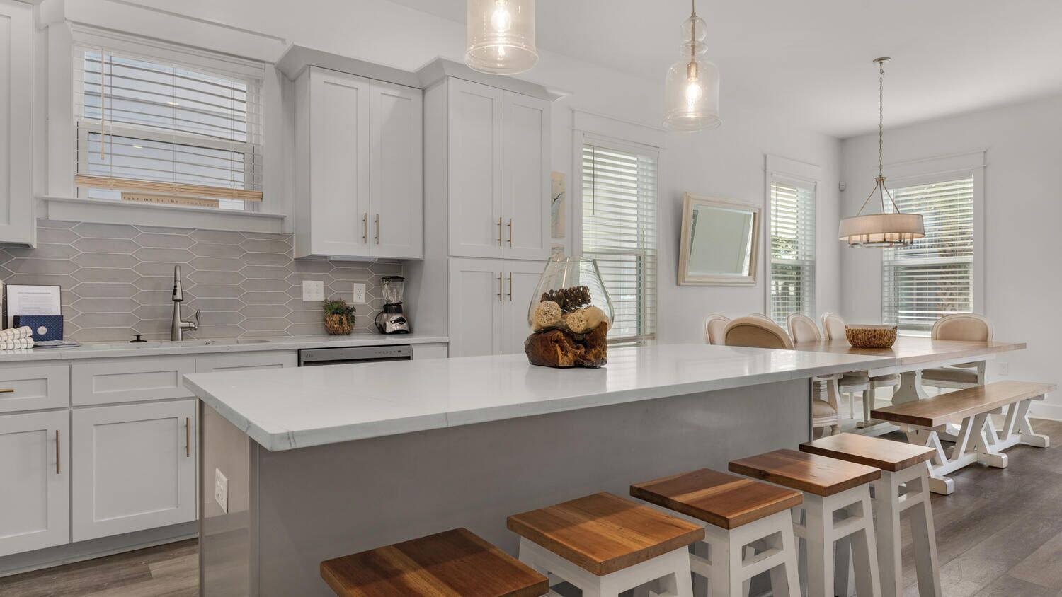 A modern kitchen with white cabinets, a large island with stools, and pendant lighting.