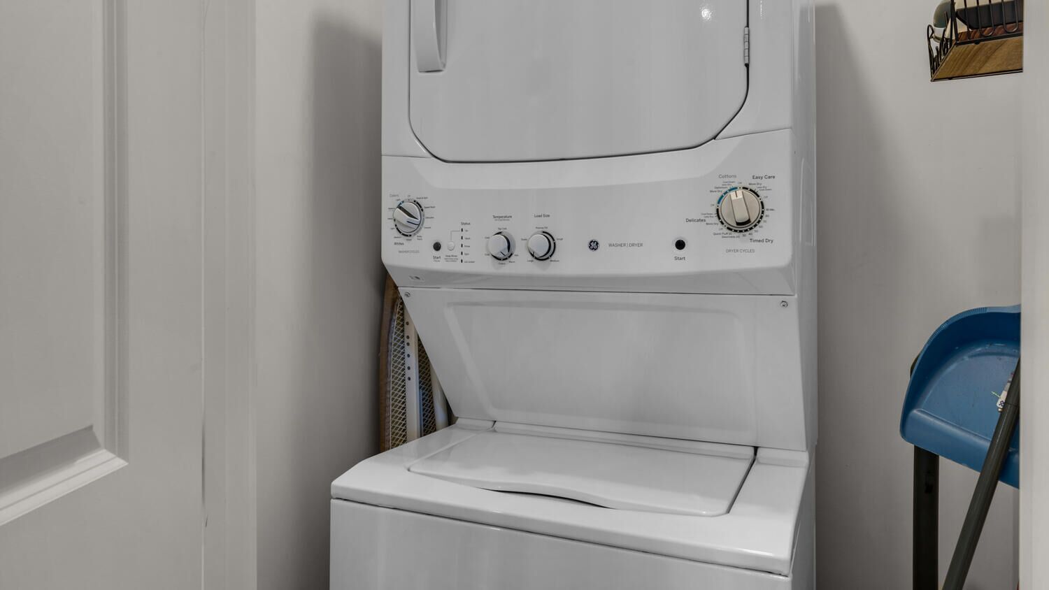 A front-loading washing machine with control panel, located in a laundry room with a blue chair.