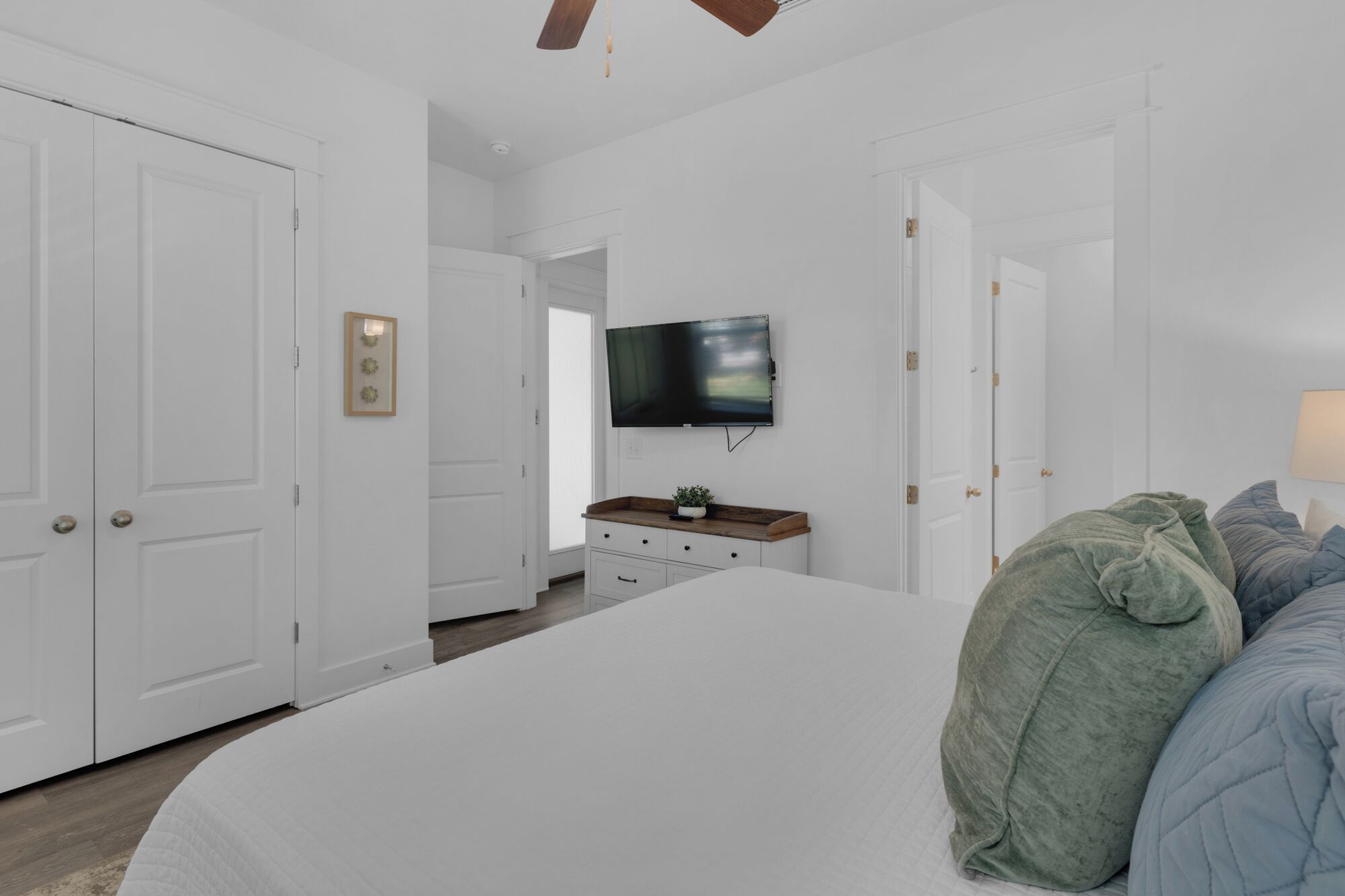 A bedroom with a large bed, a TV mounted on the wall, and a wooden dresser.