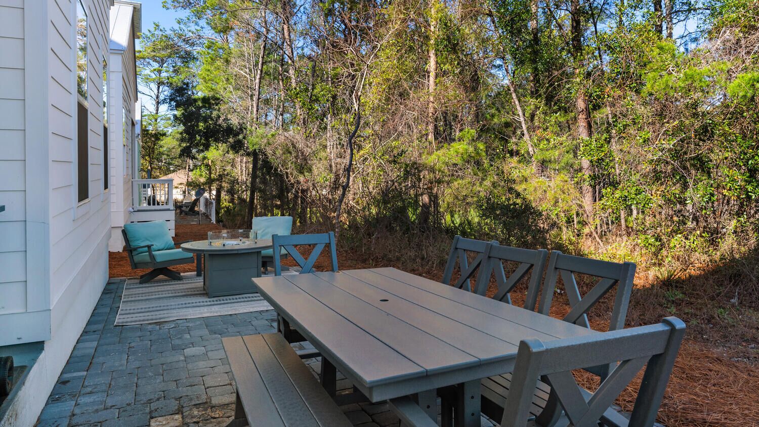 An outdoor patio with a wooden table and chairs, surrounded by trees.