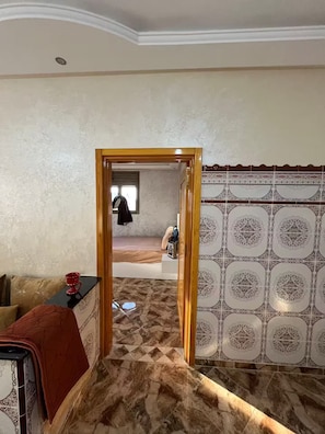 A room with a patterned tile wall, a wooden door frame, and a bed with a patterned bedspread.