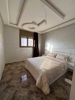 A bedroom with a large bed, a nightstand, a window with curtains, and a ceiling light fixture.