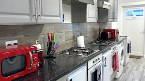 A modern kitchen with grey cabinets, a red microwave, a gas stove, and a built-in oven. - King Studio (Romford)