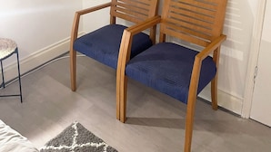 A room with two wooden chairs with blue cushions, a small shelf with decorative items, and three wall-mounted mirrors. - King Studio (Romford)