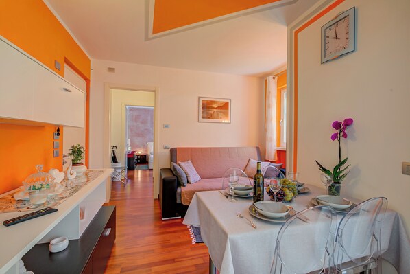 A dining area with a table set for two, a sofa, and a kitchen area with cabinets and a countertop.