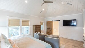 A spacious bedroom with a large bed, a TV mounted on the wall, and a sliding barn-style door leading to a bathroom. - Seagrove - Sleeps 13 - Private Pool- Near Seaside (Santa Rosa Beach)