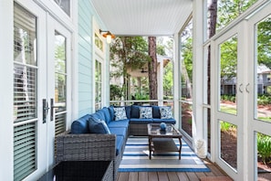 A covered porch with a blue sofa, wicker furniture, and a wooden table. - Watercolor - Watercolor Amenity Passes - Sleeps 8 (Santa Rosa Beach)