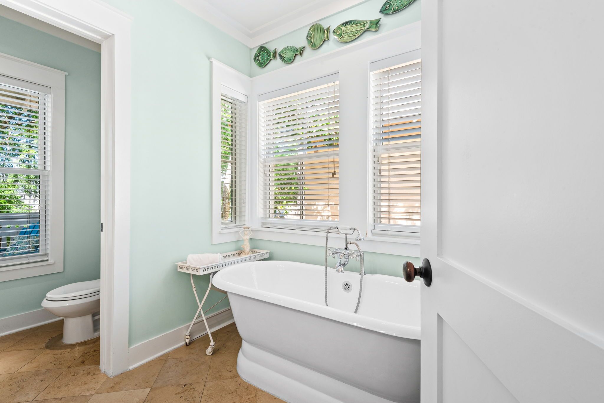 A bathroom with a freestanding bathtub, a toilet, and a window with blinds.
