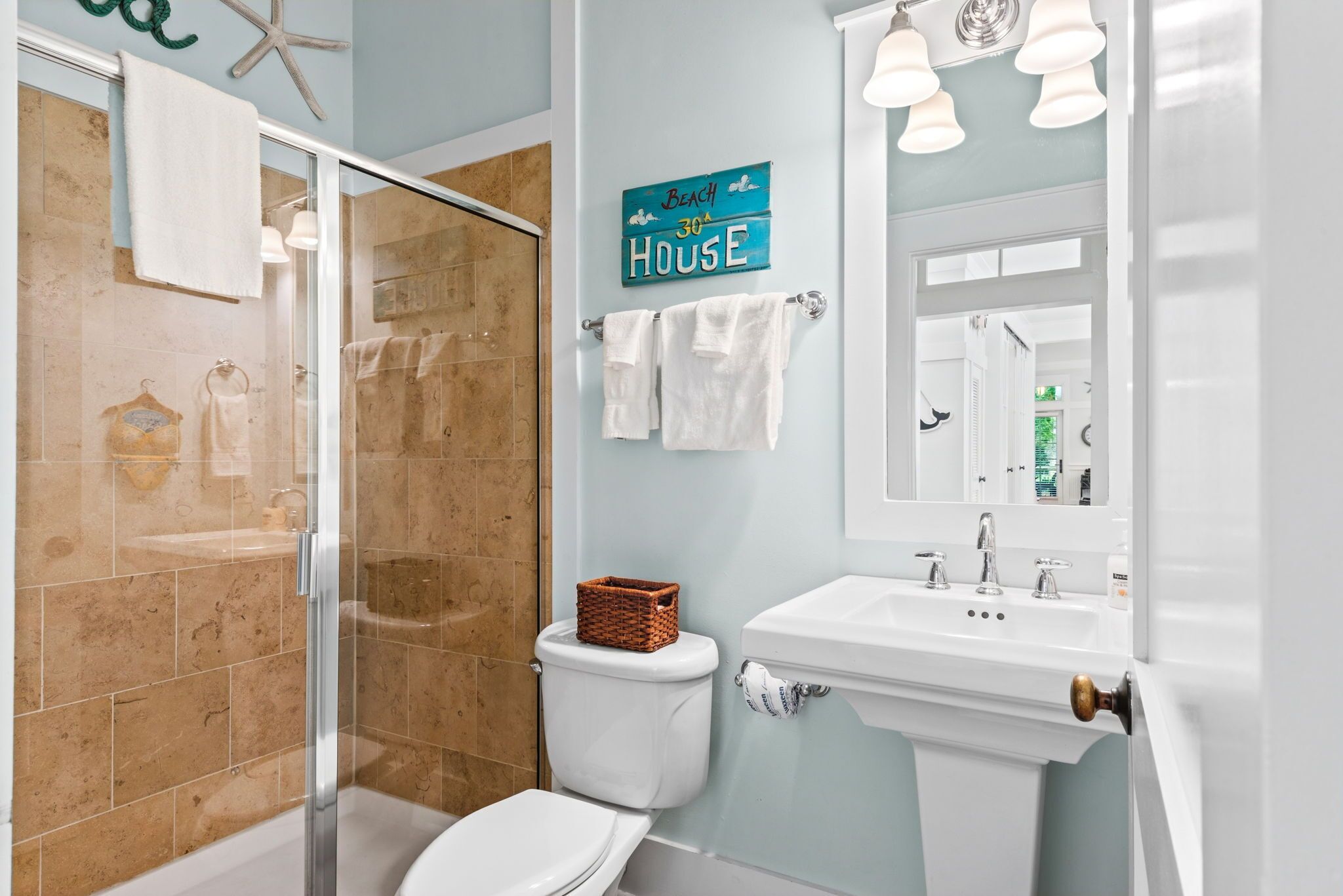 A bathroom with a glass shower enclosure, a white toilet, a sink with a mirror, and a towel rack.