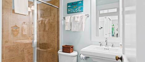 A bathroom with a glass shower enclosure, a white toilet, a sink with a mirror, and a towel rack.