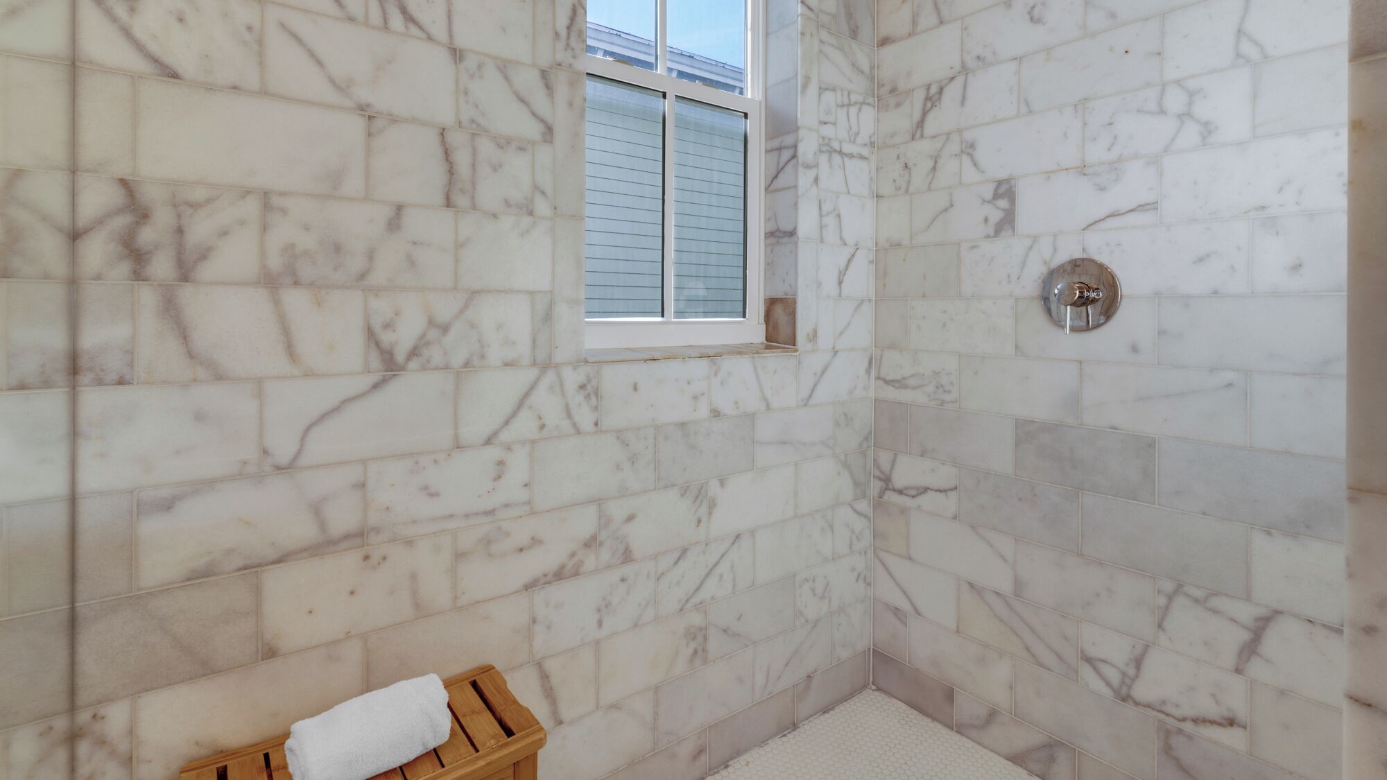 A bathroom with marble walls, a small window, and a wooden bench with a towel.