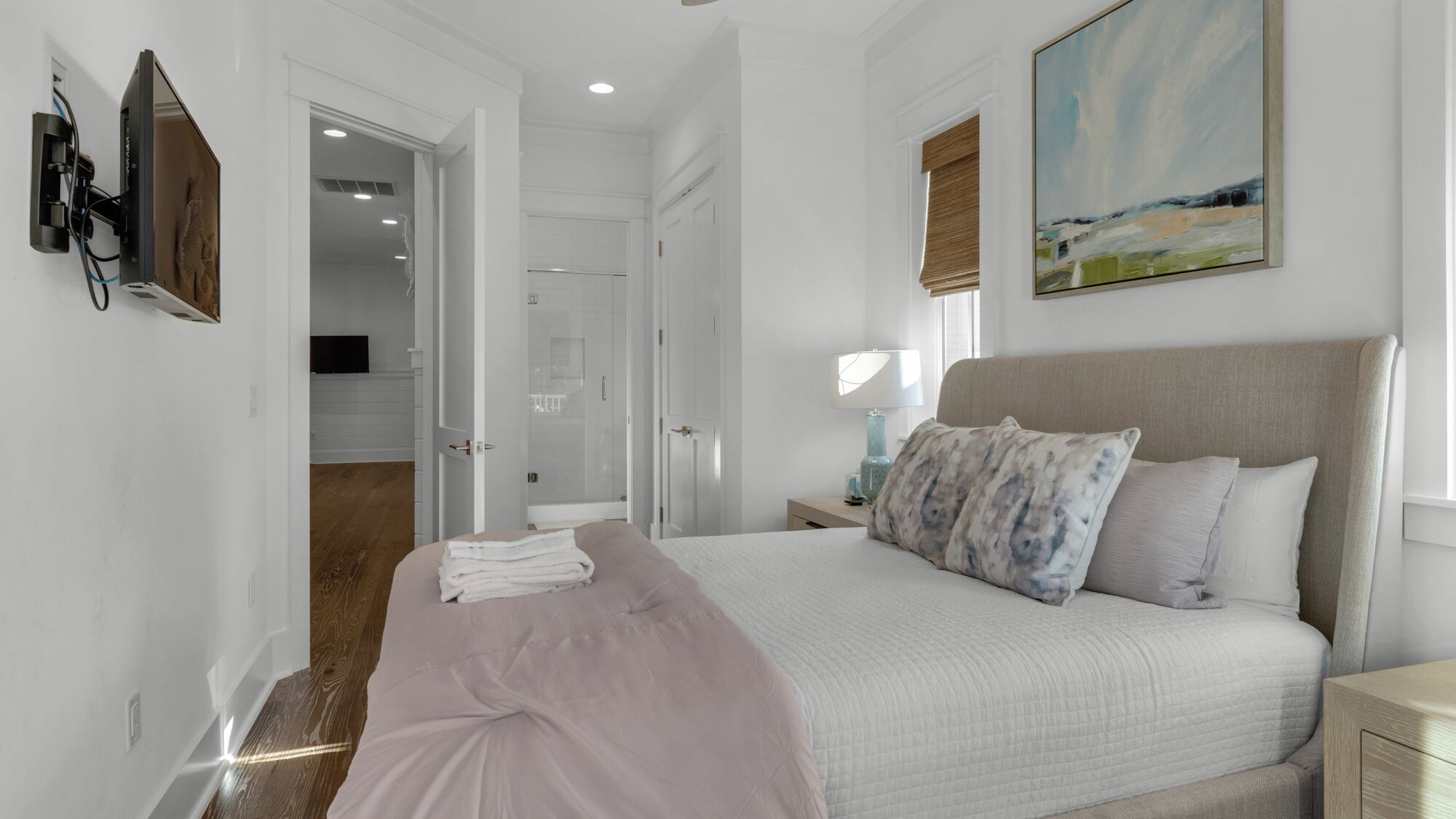 A bedroom with a bed, a nightstand, a painting, and a bathroom visible through an open door.