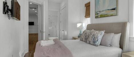 A bedroom with a bed, a nightstand, a painting, and a bathroom visible through an open door.