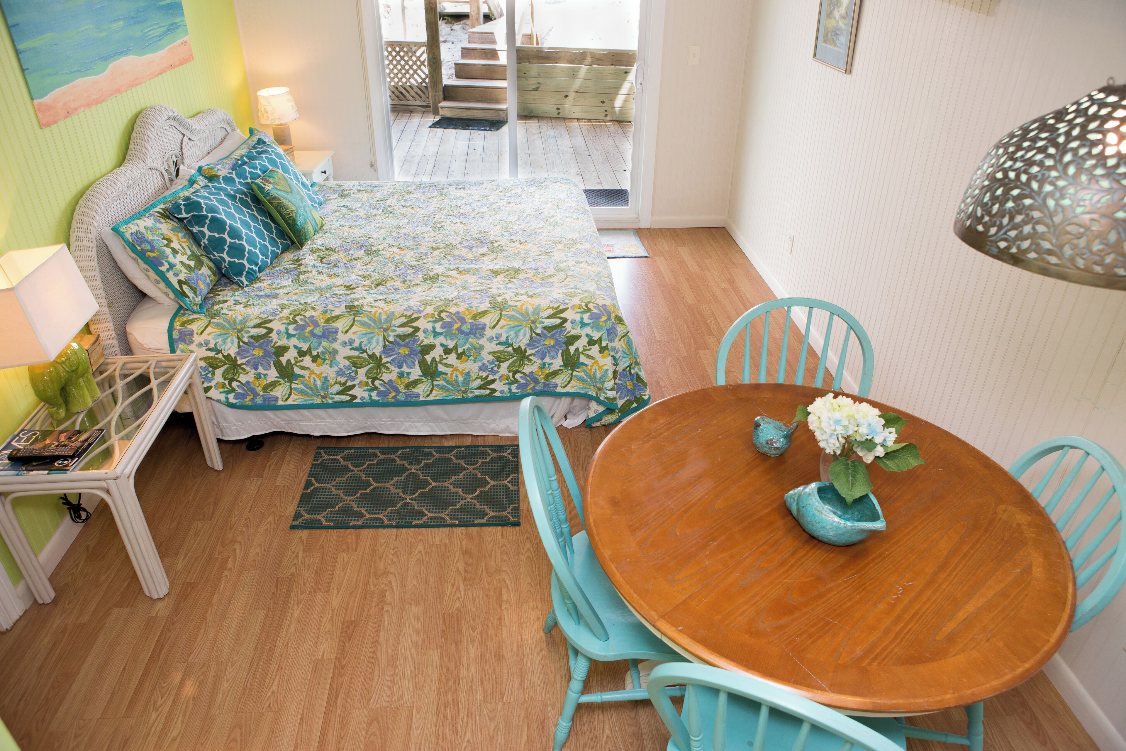 A bedroom with a bed, bedside table, lamp, and a view of the outside.