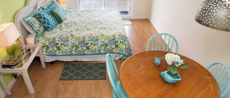 A bedroom with a bed, bedside table, lamp, and a view of the outside.