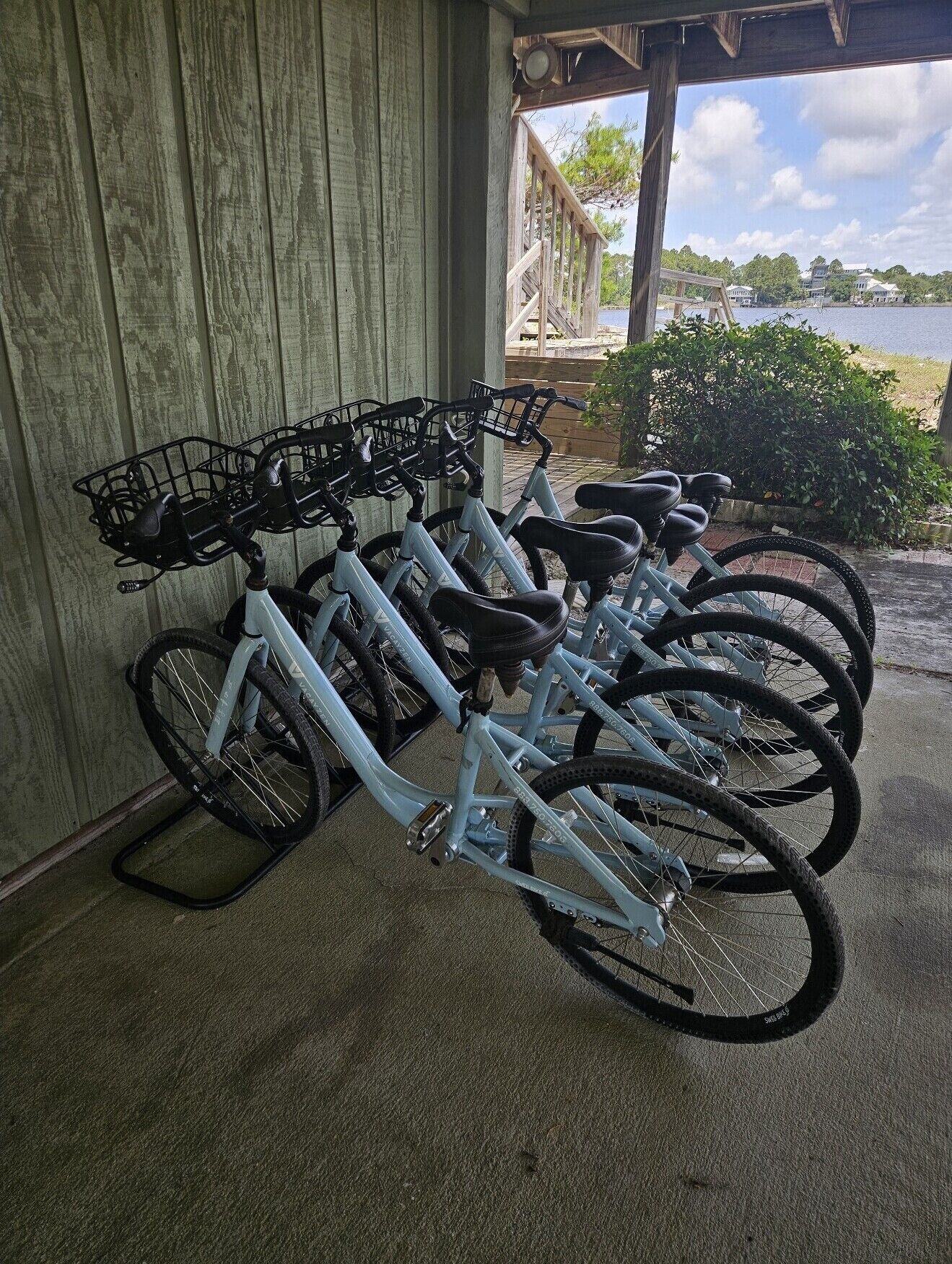 A row of bicycles parked against a wooden wall, with a view of a lake and buildings in the background.