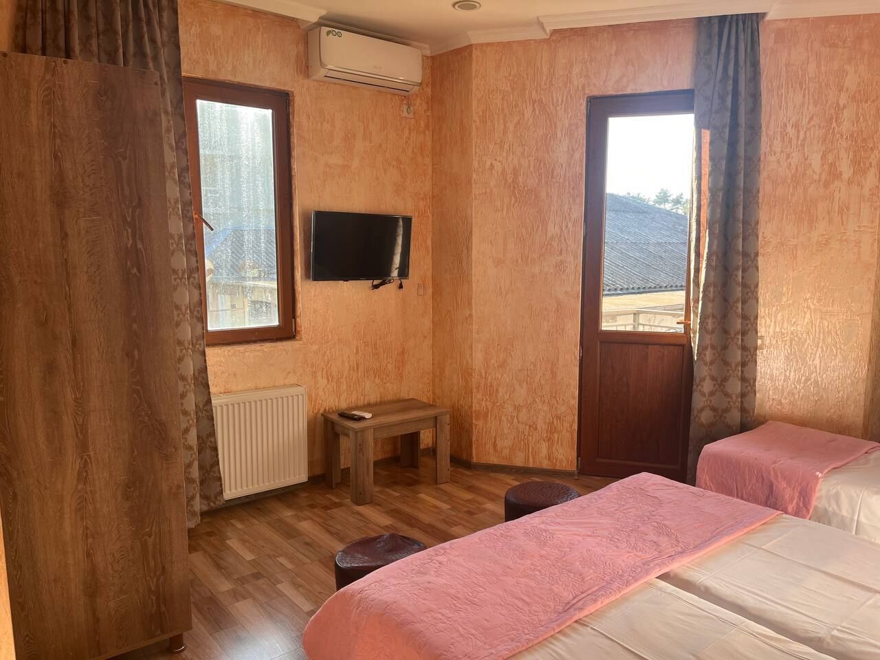 Une chambre avec deux lits, une petite table, un téléviseur et une fenêtre avec des rideaux.
