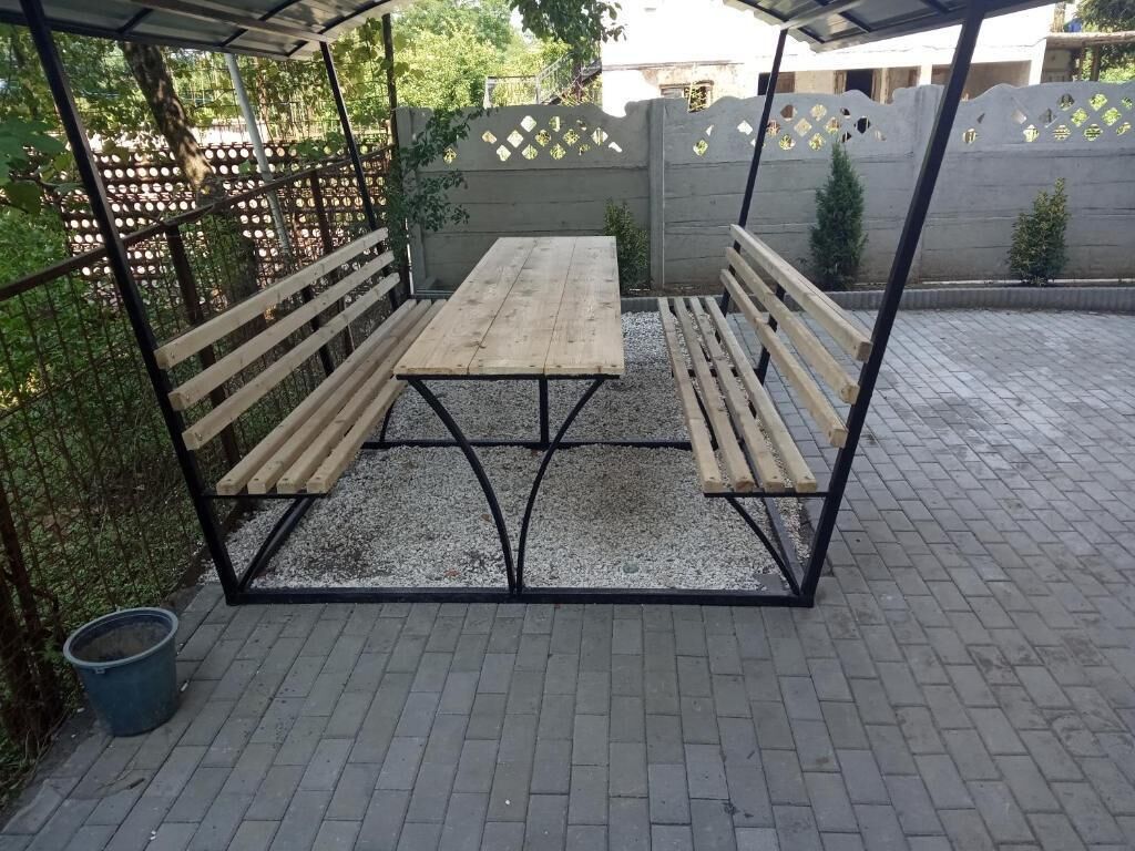A wooden bench and table set up under a metal frame structure with a gravel floor.