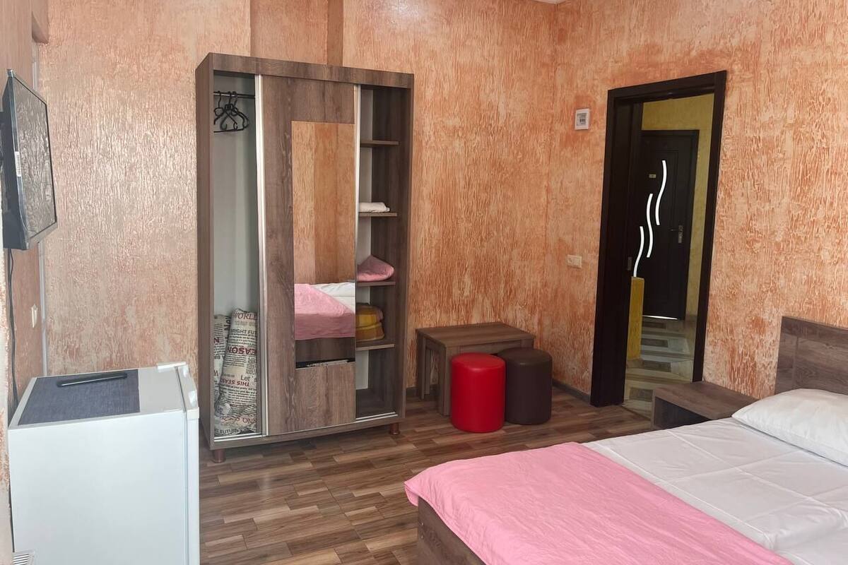 A bedroom with a bed, a wardrobe, a small table, and a red stool.