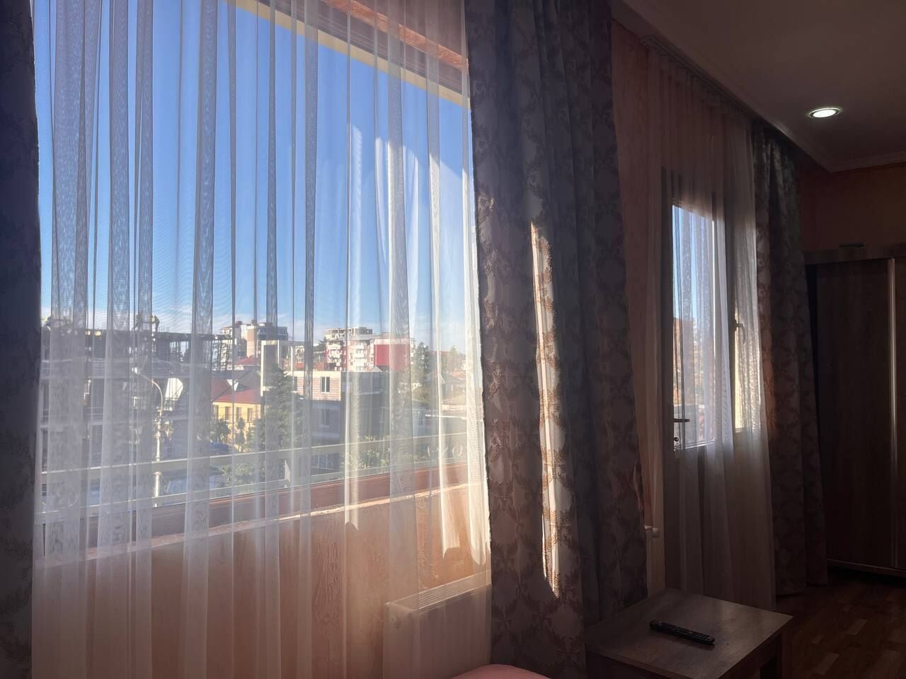 Una habitación con ventanas amplias, vistas a edificios y una pequeña mesa.
