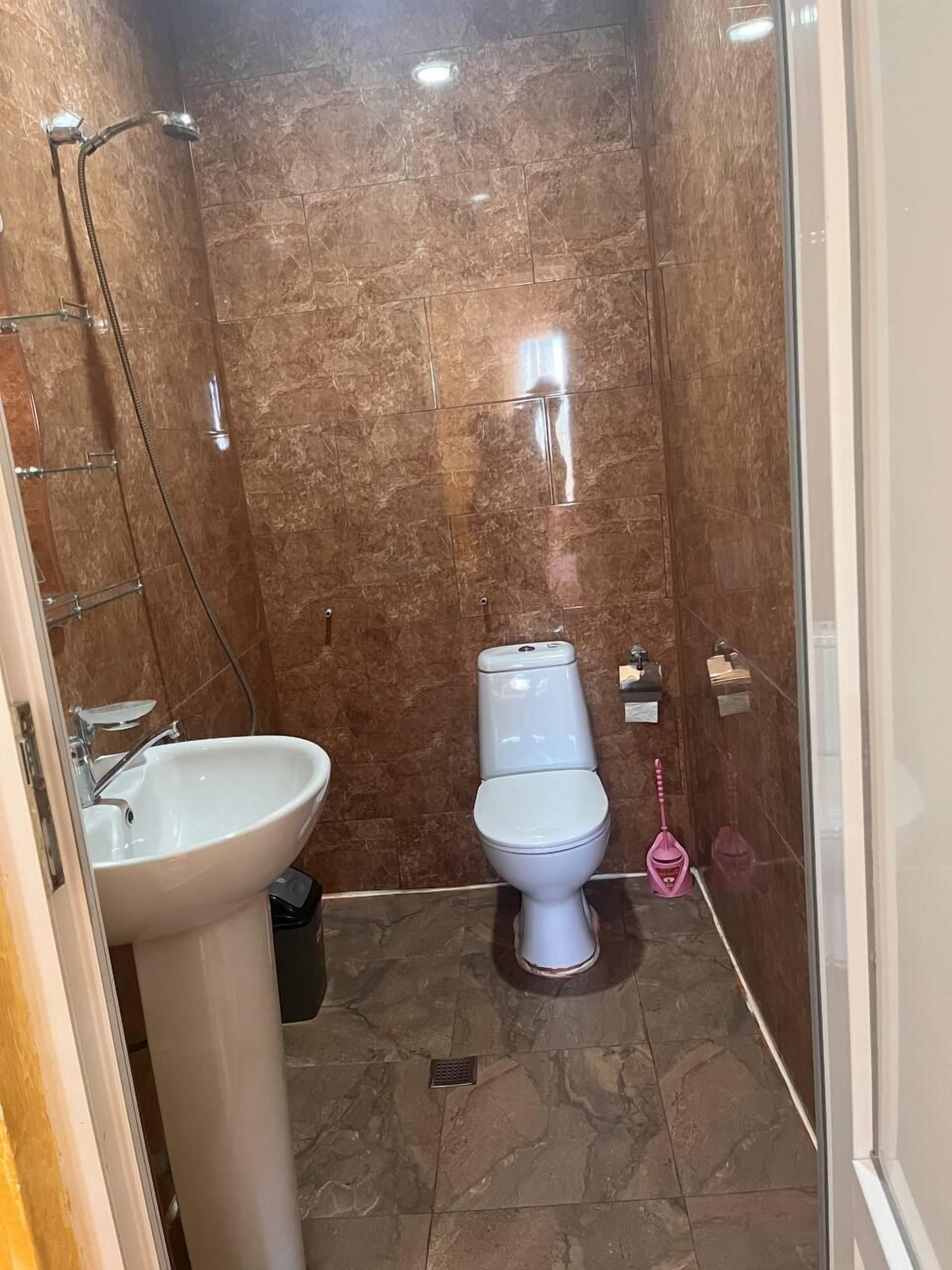 A bathroom with a marble wall, a white sink, a toilet, and a shower.