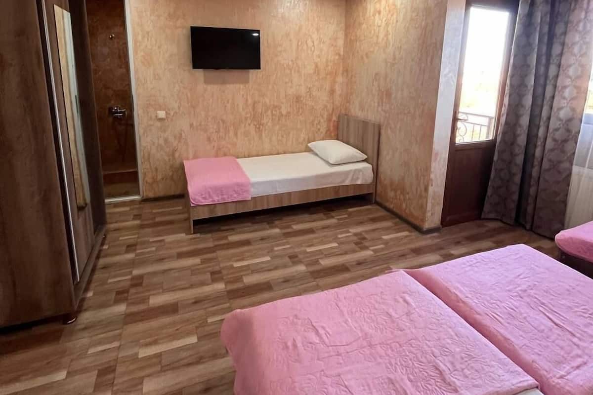 A room with a bed, a TV mounted on the wall, and a wooden floor.