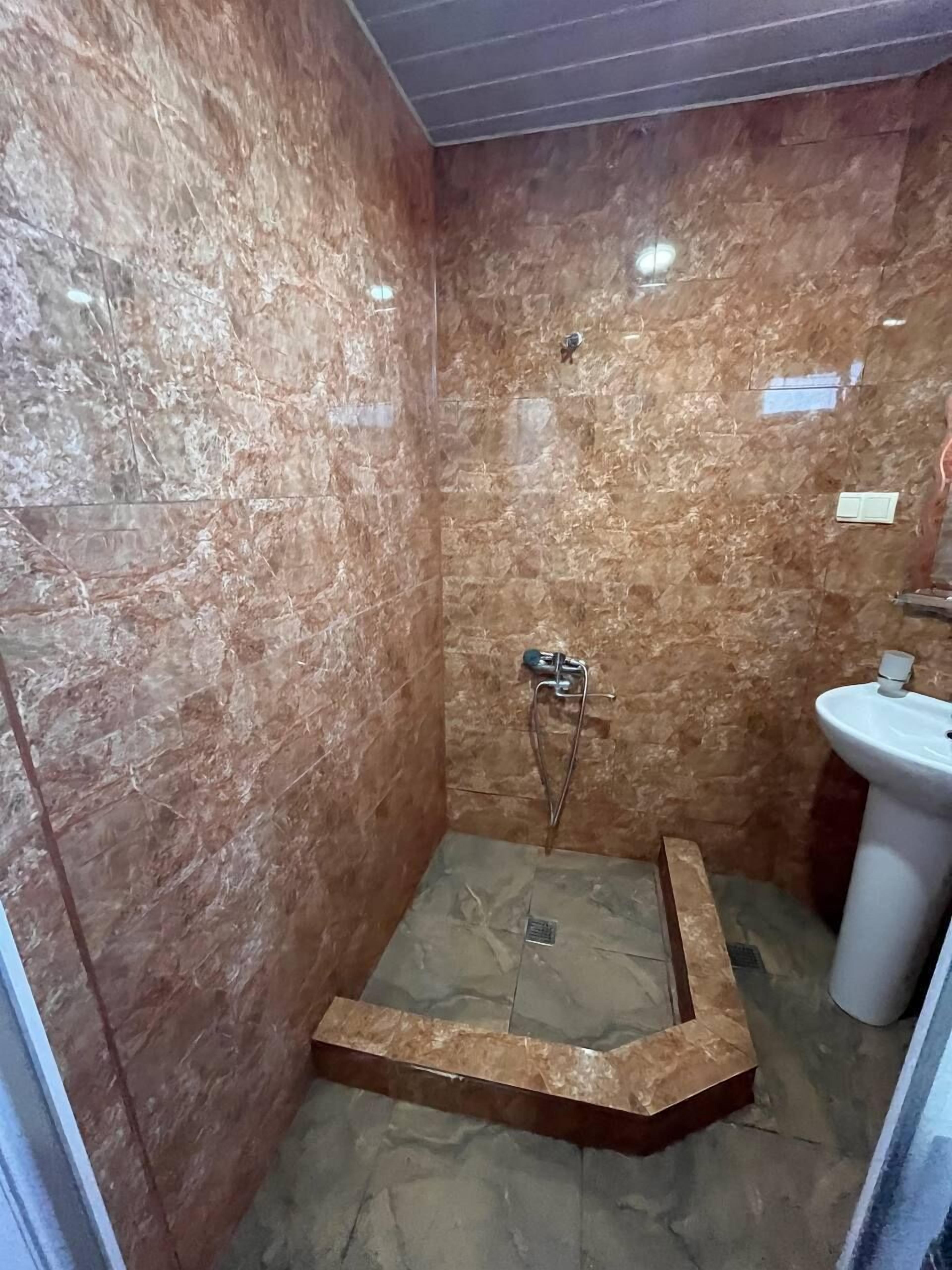 A bathroom with a shower, a sink, and marble walls.